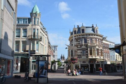 Crowds of shoppers carrying bags along a busy retail street lined with storefronts.
